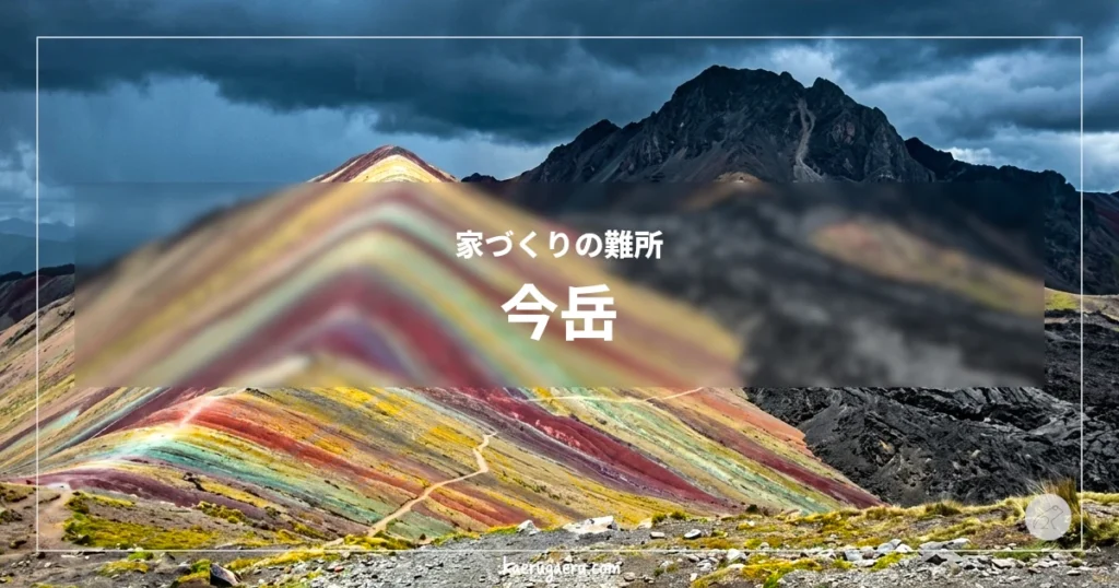 家づくりの難所 今岳。鮮やかな赤や黄色、緑の地層が縞模様を描くレインボーマウンテンと、その先にある黒い山頂と、背後に広がる暗い雲。
