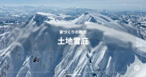 家づくりの難所 土地雪庇。青空の下、巨大な雪庇が形成された険しい雪山の稜線と、遠くに連なる山々。