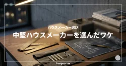 デスクライトに照らされたモダンな書斎の机。アンティーク調の金属製メジャーや、丸められた青い建築図面、プレカット木材、コンクリートブロック、ペンケースが並ぶスタイリッシュな作業風景。「ハウスメーカー選び 中堅ハウスメーカーを選んだワケ」の文字タイトル入り。