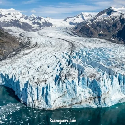 雪山の間を通り海へと流れ込む巨大な氷河。手前には切り立った青白い氷の壁が広がっている。